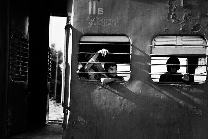Черно-белая документальная фотография мальчиков, выглядывающих из окна поезда. Естественное кадрирование фотографии.