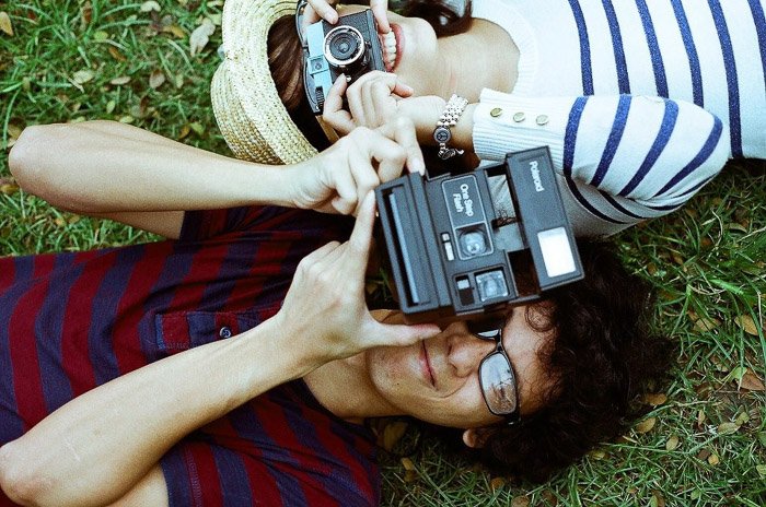 Снимок сверху двух людей, лежащих на траве и нацеливших камеры на фотографа. Советы Instagram для начинающих фотографов.