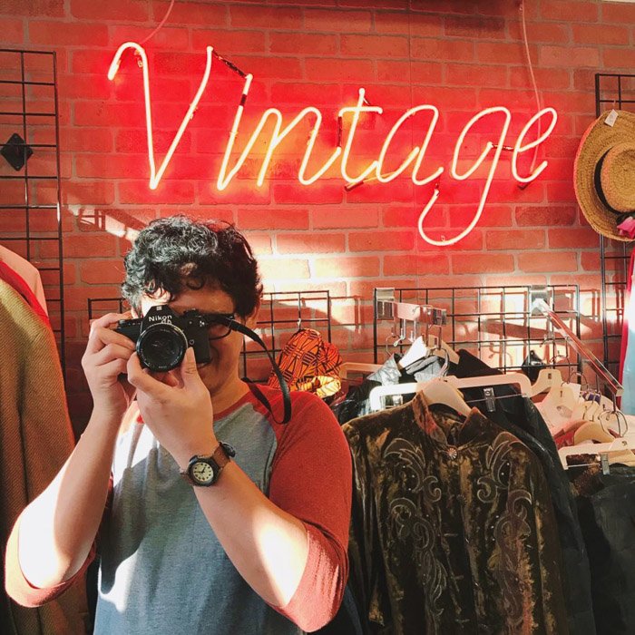 Портретная съемка мужчины в магазине винтажной одежды с фотоаппаратом в руках. Советы по фотографии в социальных сетях.