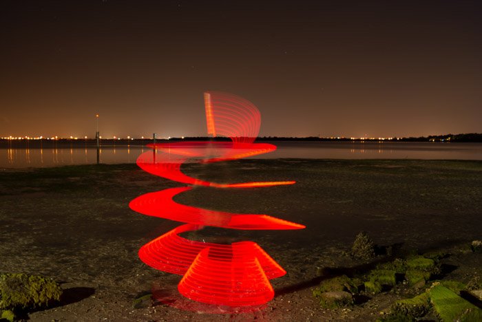 Спираль красного света, освещающая фотографию на пляже ночью.