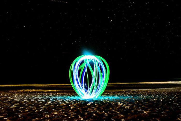 Зеленый и голубой свет рисует шар на пляже ночью.