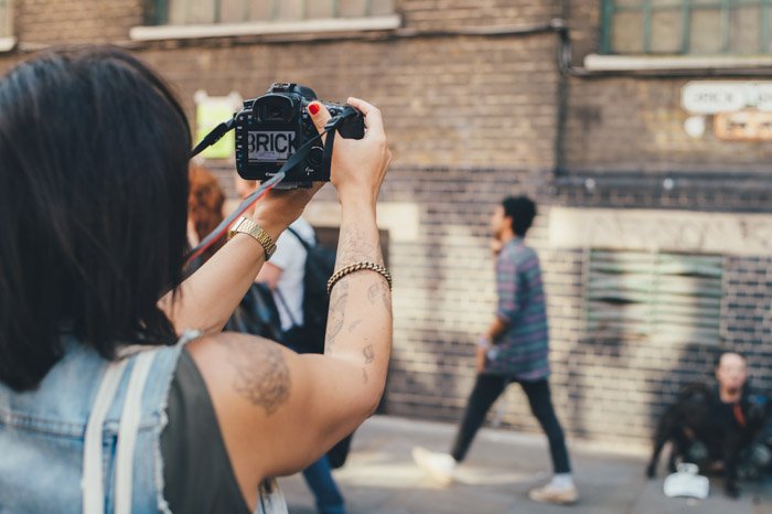 Женщина-уличный фотограф держит в руках зеркальную камеру и делает откровенные снимки прохожих