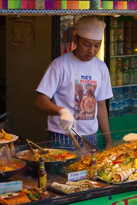 Мужчина готовит мексиканскую еду в киоске на рынке Камден. 