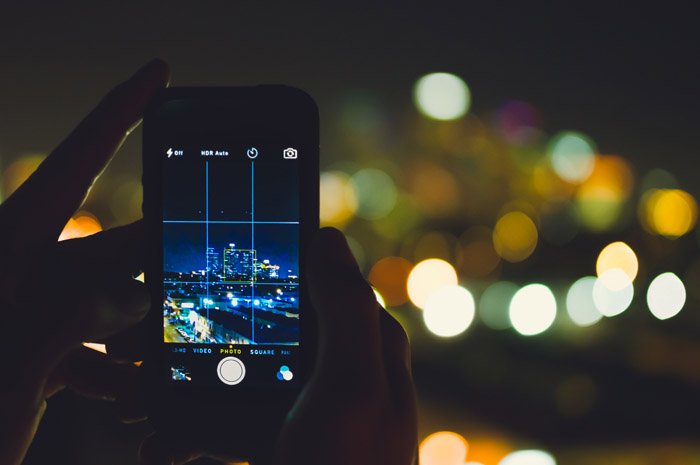Человек снимает уличную фотографию ночью со смартфона