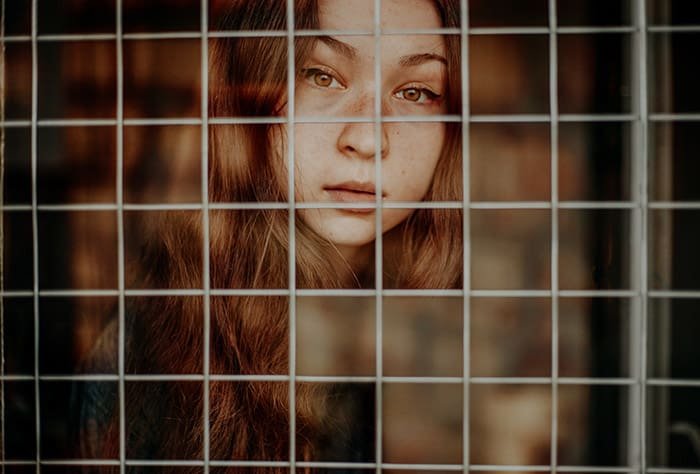 A cut out photo portrait of a brown haired girl behind a chain fence