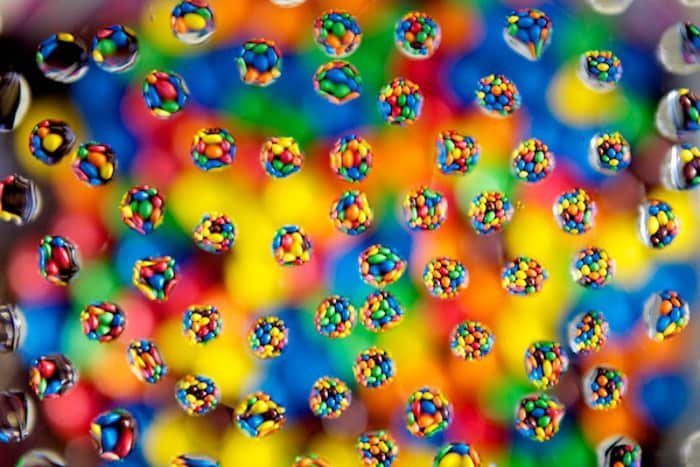 Забавная фотография капель воды с кругами из ярко окрашенных конфет с каплями на фоне боке 