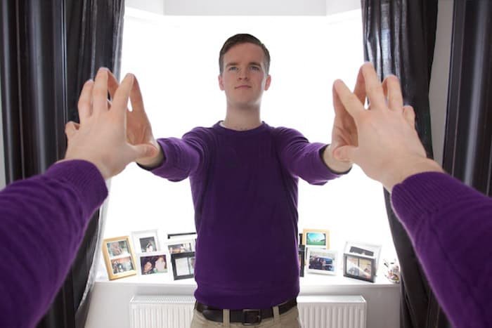 Мужчина в фиолетовом джемпере касается руками своего отражения в зеркале