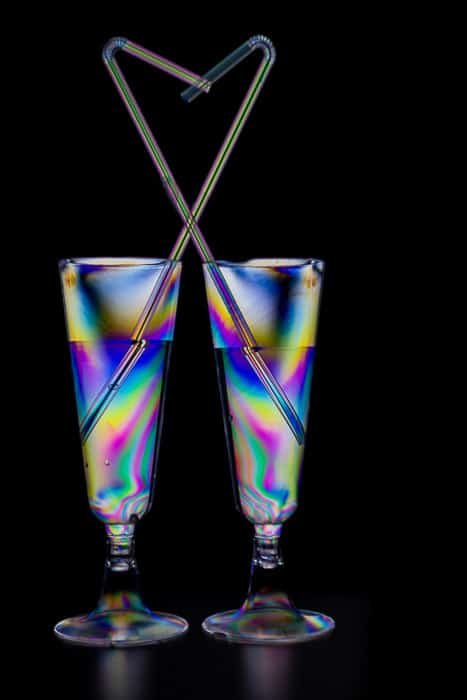Два коктейльных бокала, наполненных разноцветным эффектом фотоэластичности на черном фоне
