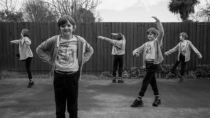 Черно-белая широкоугольная многоплановая фотография пяти одинаковых маленьких девочек, танцующих на улице