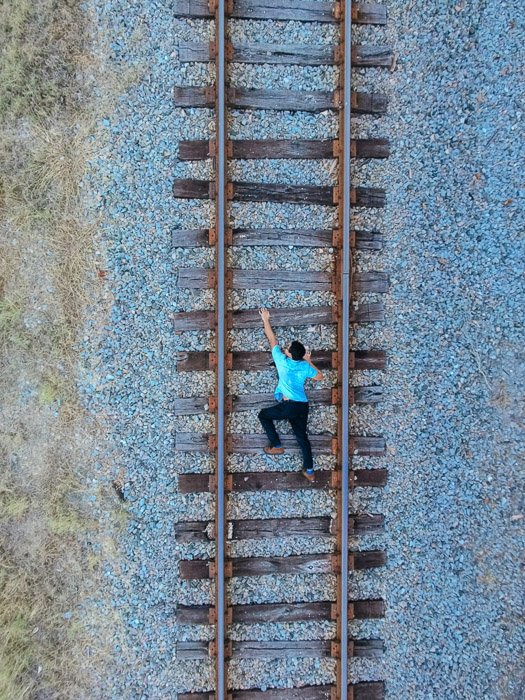 Фотография человека на железнодорожных путях, сделанная сверху, чтобы создать иллюзию, что он поднимается вверх