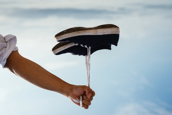 Человек держит пару ботинок за шнурки, которые выглядят так, будто они плавают, как воздушный шар