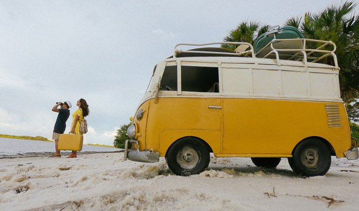 Пара на пляже с желтым фургоном позади них