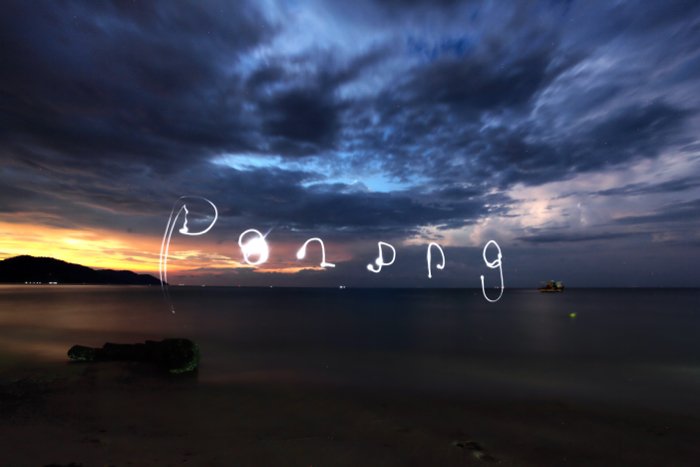 Слова, нарисованные в небе над морским пейзажем ночью, с помощью фонарика смартфона для рисования светом