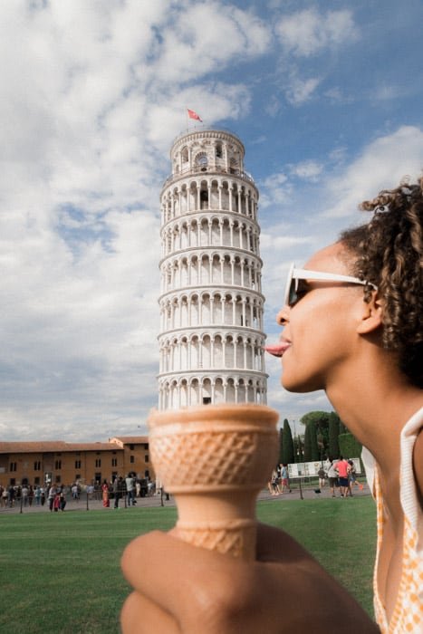 Веселая фотография с вынужденной перспективой, на которой девушка позирует так, чтобы казалось, что она облизывает Пизанскую башню в рожке мороженого
