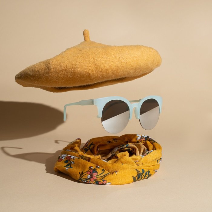 Крутой пример стилизации товарной фотографии левитирующей пары солнцезащитных очков под беретом и поверх шарфа