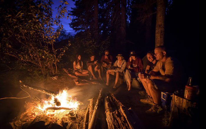 Группа людей сидит вокруг костра в лесу ночью