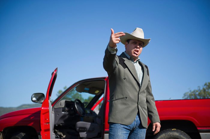 Мужчина в ковбойской шляпе стоит перед красным автомобилем и делает жест рукой - чаевые за фотографии людей