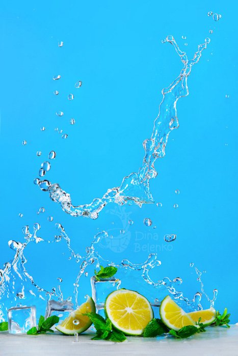  Долька лайма, лед, листья мяты и динамичный всплеск воды для мохито или лимонада на ярко-синем фоне. Концепция освежающего летнего напитка с пространством для копирования.