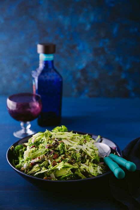 Food styling: Миска с нарезанным салатом броколли, бальзамический венгер и маленький бокал на темно-синем фоне