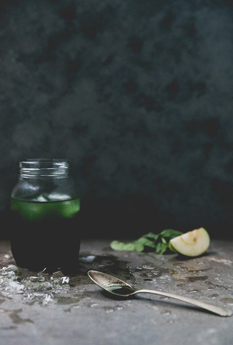 Советы по стилизации блюд: Натюрморт с зеленым напитком в банке, чайной ложкой и ингредиентами на темном фоне