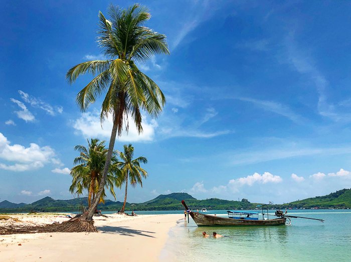 Мечтательная сцена тропического пляжа с пальмами и деревянной лодкой