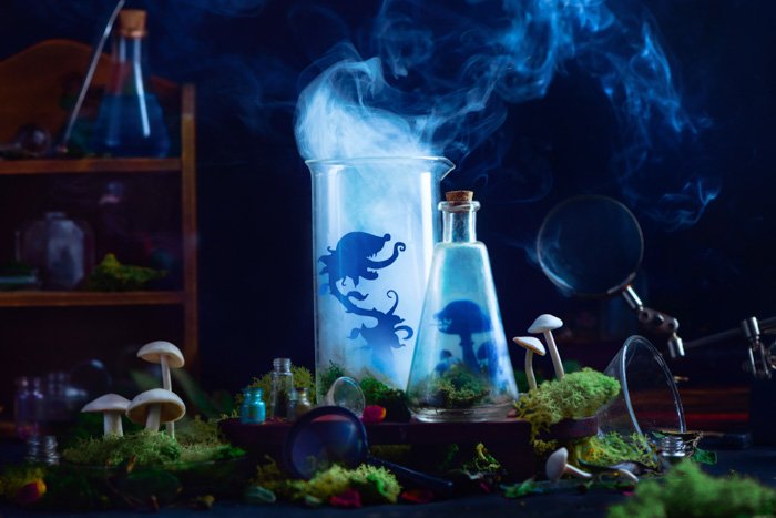 Мистический натюрморт с изображением стеклянных бутылок с силуэтами крошечных вырезанных персонажей внутри и выходящим дымом