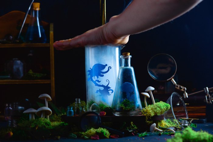 Настройка для съемки дымового натюрморта с изображением стеклянных бутылок с силуэтами крошечных вырезанных персонажей внутри и выходящим дымом