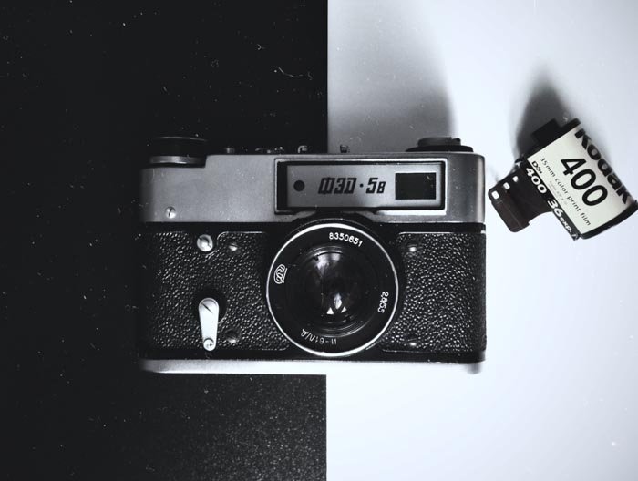 Снимок сверху старой пленочной камеры на черно-белом фоне с рулоном пленки рядом - использование пленки для уличной фотографии