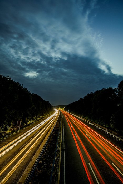 Вид ночного шоссе с цветными потоками световых следов от автомобилей, снятый с использованием 180 правил размытия движения