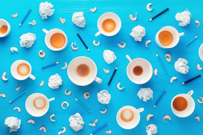 Рабочее место творческой профессии с пустыми кофейными чашками, смятыми бумажными шариками и карандашными стружками на красочном синем фоне. Минималистская концепция вдохновения с использованием оранжевой и синей цветовой схемы