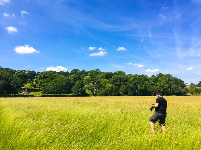 человек с камерой идет по полю ярко-зеленой травы под глубоким синим небом