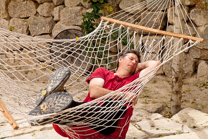 мужчина в красной рубашке спит в гамаке на открытом воздухе, позади него скалистая стена