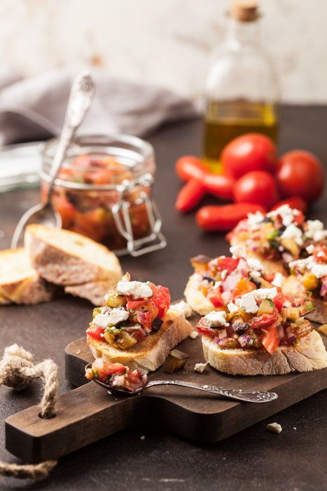 Закуска брускетта подается на деревянном подносе, с помидорами и баночкой оливкового масла рядом