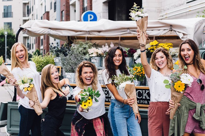 Веселая групповая фотография девушек, держащих букеты цветов и улыбающихся