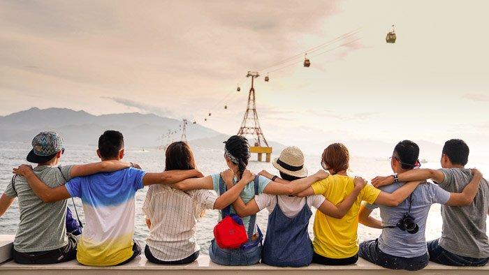 Веселая групповая фотография 6 друзей, обнявших друг друга и смотрящих на океан