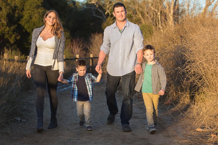 Портрет семьи из 4 человек, улыбающейся и держащейся за руки во время прогулки на природе