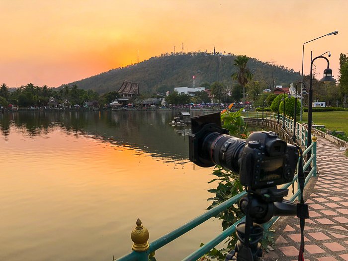 Камера, установленная на штативе на берегу, смотрит на горы, море и горизонт в золотом закате - How to Take Stock Photos That Sell