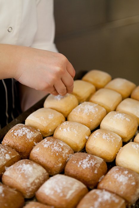 close up of baker's hand spring sugar on newly baked buns