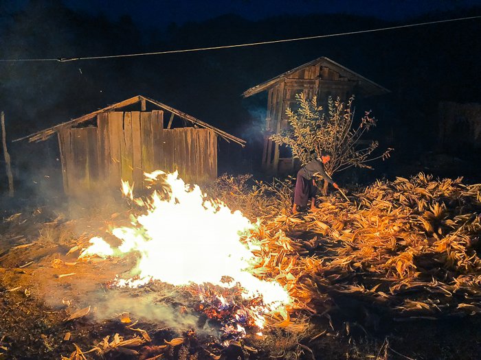 фото женщины, сгребающей листья в костер возле деревянного домика ночью