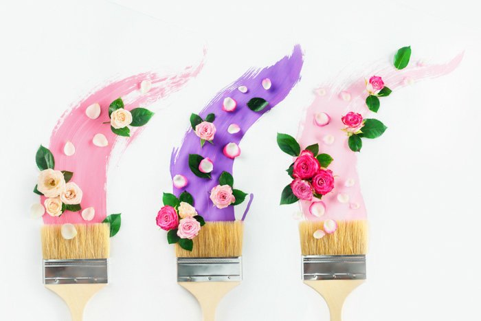 Кисти с красками розовых и фиолетовых оттенков, розы и лепестки, на белом фоне. Живопись весна творческий плоский слой. Концепция украшения дома.