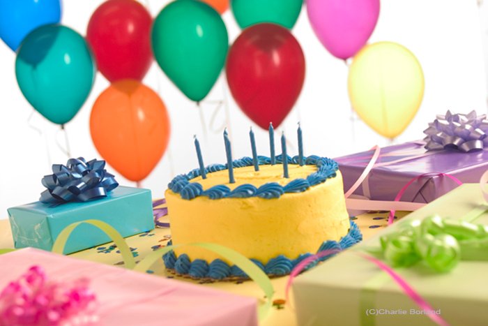 Снимок натюрморта с праздничным тортом, воздушными шарами, подарками, завернутыми в бумагу разных цветов, и праздничными серпантинами