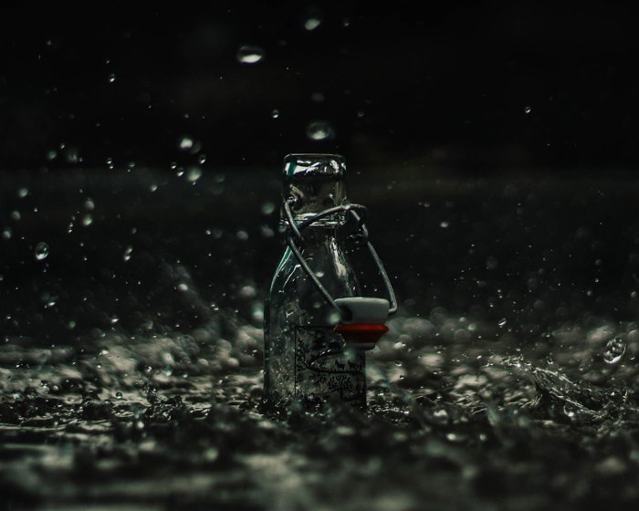 Атмосферная фотография стеклянной бутылки, обрызганной падающим дождем