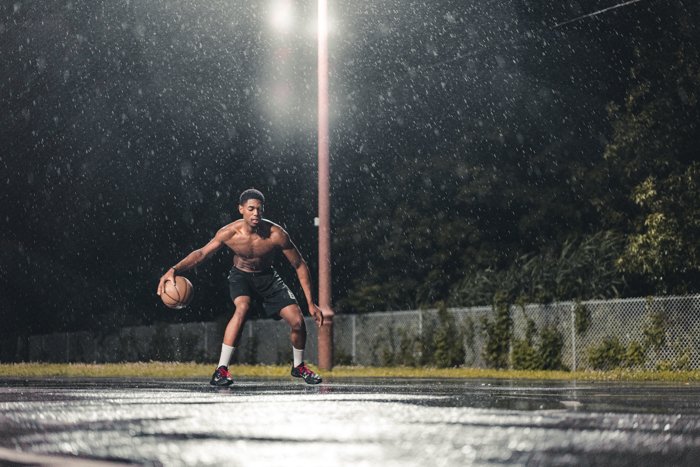 Атмосферный дождь фотографирует человека, играющего в баскетбол ночью