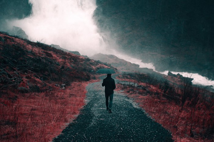 Dark and moody rain image of the person walking through a landscape with an umbrella