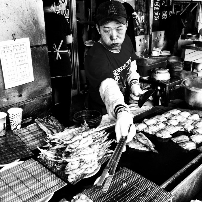 черно-белая уличная фотография продавца на рынке, жарящего рыбу