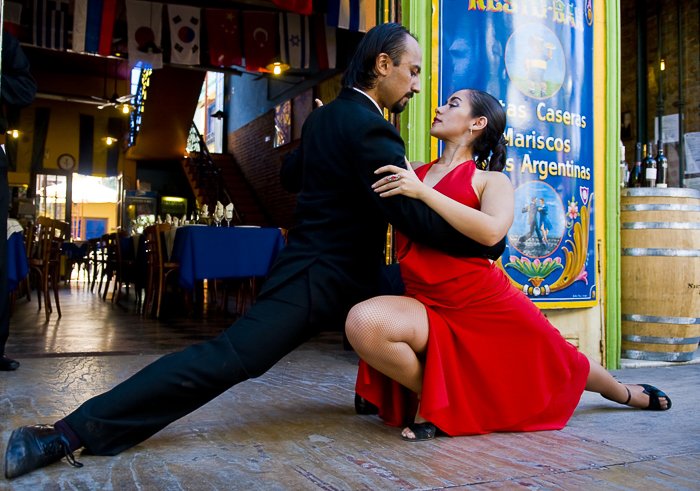 мужчина и женщина в красном платье пристально смотрят друг на друга, исполняя танец