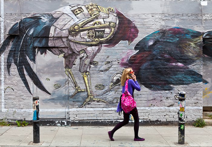 Девушка-блондинка в розовом шарфе, разговаривающая по телефону, проходя мимо стены с граффити стрит-арт - путешествия фото направлений