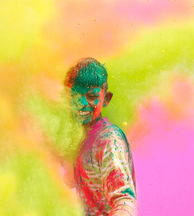 мальчик, покрытый разноцветными красками, стоит в облаке цветов на фестивале