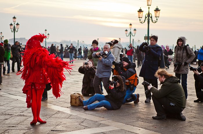 люди фотографируют уличного артиста в пернатом красном наряде