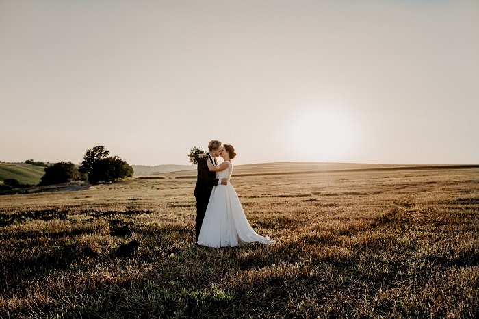 Жених и невеста целуются в поле на закате